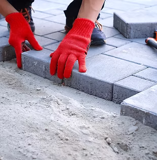 The master in yellow gloves lays paving stones in layers_ Garden brick pathway paving by p